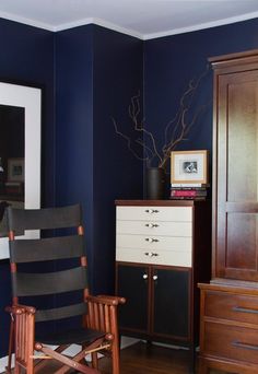 a chair and dresser in a room with dark blue walls, wood floors and white trim