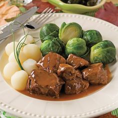 a white plate topped with meat and brussel sprouts next to potatoes