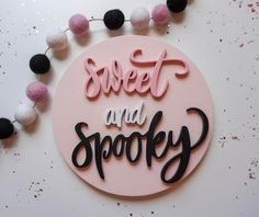 a pink and black sign that says sweet and spooky with pom - poms around it