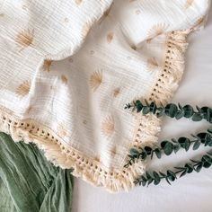 an unmade bed with white sheets and green leaves on the pillowcase, next to a plant