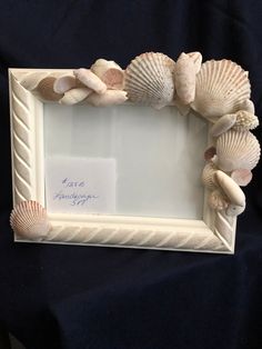 a white frame with seashells on it and a note attached to the front