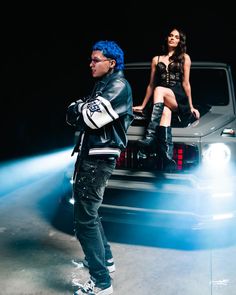 two people sitting on the back of a car in front of a woman with blue hair