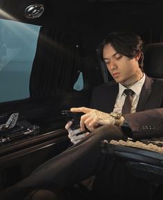 a man in a suit and tie sitting in a car looking at his cell phone