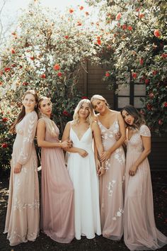 a group of women standing next to each other in front of a bush with red flowers