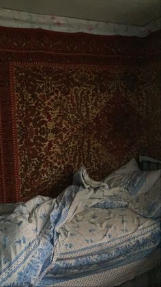 an unmade bed with blue and white comforter in front of a red wall