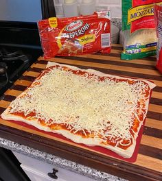 an uncooked pizza sitting on top of a wooden cutting board next to bags of cheese