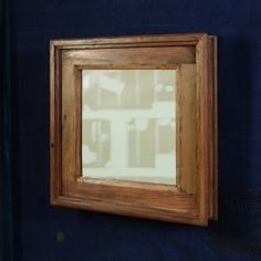 an old wooden framed mirror hanging on the wall in front of a dark blue wall