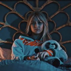 a woman laying in bed with a stuffed animal next to her chest and looking at the camera