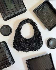 several black trays with various items in them on a white surface, including an object made out of plastic