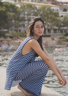 a woman in a blue and white dress sitting on the edge of a body of water