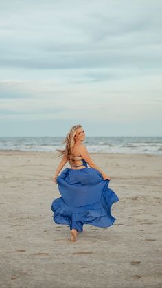 a woman in a blue dress is walking on the beach