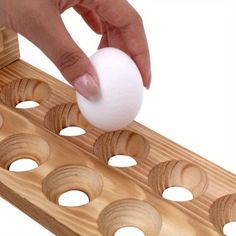 a person is placing an egg into a wooden board with holes in it and one hand