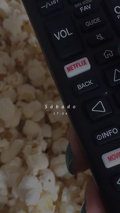 a hand holding a remote control over a pile of popcorn