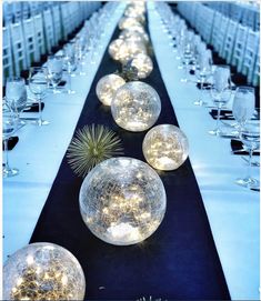 a long table is set up with clear glass balls and lights on the top one