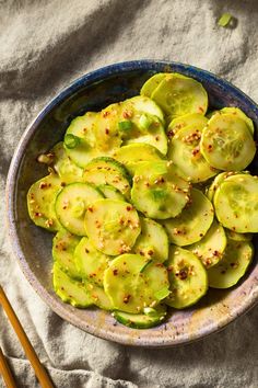 a bowl filled with sliced cucumbers next to chopsticks