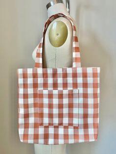 This large carryall tote is made from reclaimed fabric with a sturdy twill weave and an orange and cream gingham pattern. It features a roomy outer pocket, snap closure, and interior hook for your keys. This bag can easily hold a laptop, books, and other daily essentials. Perfect for a summer picnic or a fall day.  During the design process, clothing companies use and discard an enormous amount of fabric. I make my products using these pre-consumer materials. Your purchases give these fabrics new life and prevent them from being discarded and sent to a landfill. Thank you for your support! Measurements: 15"x17" Materials: Burn-tested mixed synthetic fabric. Fabric and hook are reclaimed materials, snap closure is new material. Everyday Orange Bags With Pockets, White Cotton Bag For Picnic, White Cotton Picnic Bag, White Cotton Picnic Bags, Rectangular Cotton Gingham Bags, Rectangular Gingham Cotton Bags, Gingham Cotton Bags For Everyday Use, Orange Cotton Bags For Everyday Use, Orange Cotton Bag For Everyday Use