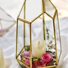 a candle is in a glass container with flowers and candles on the table next to it