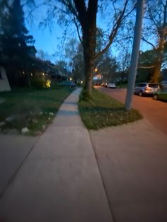 the sidewalk is lined with green grass and trees at night, as well as cars parked on the street