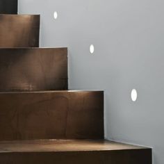 some white lights are on the side of a set of stairs in front of a gray wall