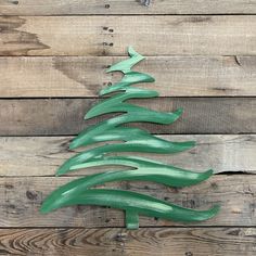 a green metal christmas tree on top of a wooden table next to a wood plank wall