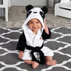 a baby in a panda costume sitting on the floor with a towel around his head