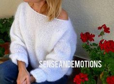 a woman in white sweater sitting on the ground next to flowers and potted plants