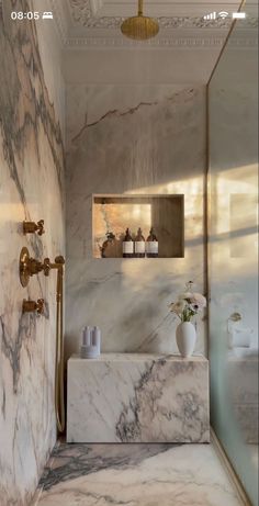 a bathroom with marble walls and flooring in the shower area, along with two gold faucets