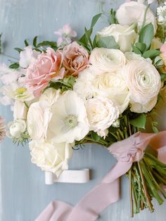 a bouquet of white and pink flowers on top of a blue door with a pink ribbon