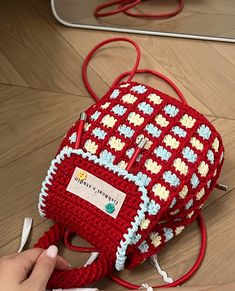 a crocheted red and white purse sitting on top of a wooden floor next to a mirror