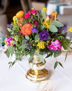 a vase filled with colorful flowers sitting on top of a white tablecloth covered table