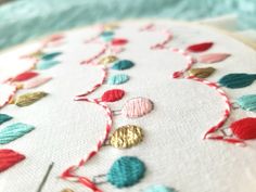 a close up of a embroidery on a white cloth with red, blue and green leaves