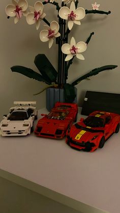 three toy cars sitting next to each other in front of a vase with orchids