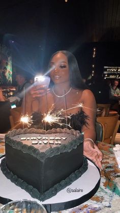 a woman sitting in front of a black cake with sparklers on it while holding a cell phone