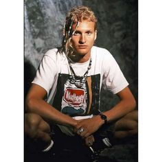 a man with dreadlocks sitting in front of a waterfall wearing a t - shirt