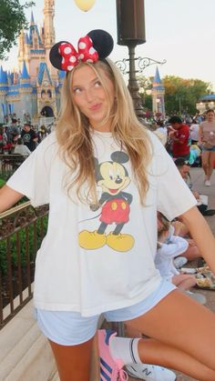 a woman posing in front of a castle with minnie mouse on her shirt and shorts