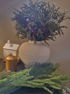 a white vase with red berries and greenery in it next to a candle holder