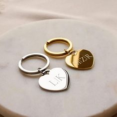 two heart shaped key chains sitting on top of a white marble table next to each other