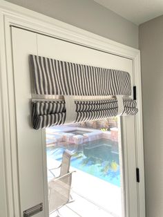 a window with roman shades on it and a pool in the background