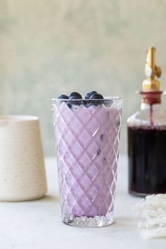 a glass filled with blueberries sitting on top of a table next to a bottle