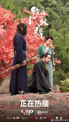 three people standing on top of a rock in front of some trees with red leaves