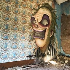 a painting of a creepy clown on the side of a wall in an abandoned building