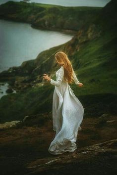 a woman in white dress standing on top of a hill