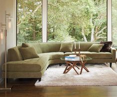 a living room with large windows and a sectional couch in front of a window that looks out onto the woods