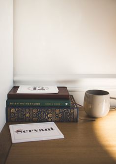 a stack of books sitting on top of a wooden table next to a coffee cup