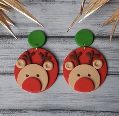 two red and green christmas themed earrings with reindeer faces on them, hanging from wooden hooks