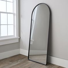 a large mirror sitting on top of a wooden floor next to a white wall and window