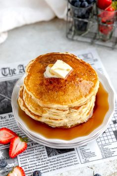 a stack of pancakes with butter and syrup on a white plate next to strawberries