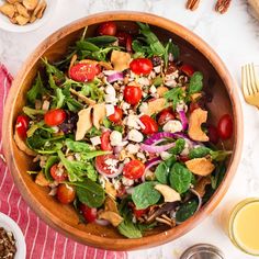 a wooden bowl filled with salad next to two bowls of nuts and other food items