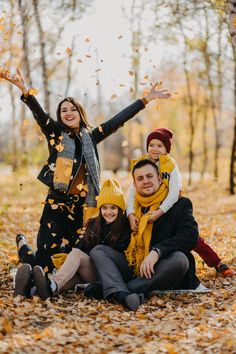 a family poses for a photo in the fall leaves with their arms up and hands out