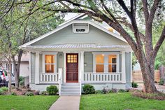 a small gray house with white trim and red front door is shown in the grass